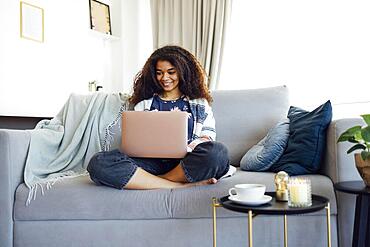 Excited cheerful young black woman using laptop computer on sofa at home, getting good news, feeling joy, doing homework or working online, laughing, happy to win prize