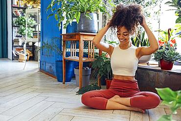 Young adult happy fit slim healthy African American ethnic woman wearing sportswear sitting in yoga pose at home in living room, doing fitness morning workout exercises training