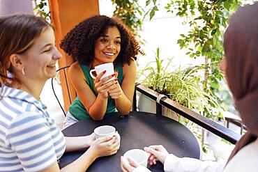 Multiethnic group of girls wearing casual clothes and traditional hijab bonding and having fun outdoors. Three young teen girls in garden cafe drinking tea or coffee