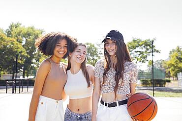 Multicultural group of young female friends bonding outdoors and having fun. Stylish cool teen girls gathering at basketball court, friends ready for playing basketball outdoors