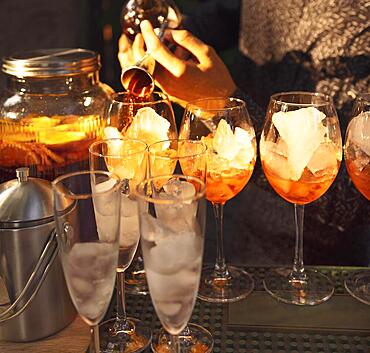 Glasses of cocktails on the bar. Bartender pours a glass of sparkling wine with red alcohol. Barman preraring aperol spritz cocktail in outdoor summer bar