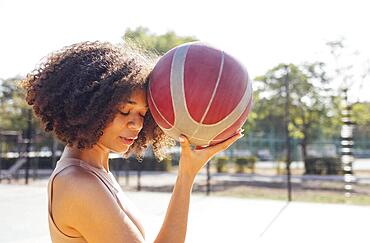 Mixed-race young smiling female outdoors and having fun. Stylish cool teen girl gathering at basketball court, playing basketball outdoors