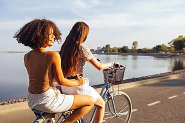 Teenagers of different nationalities and appearance on bicycles ride along a city street. Young and positive girls smile together. Healthy lifestyle and friendship concept