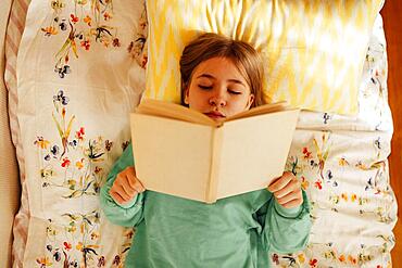 Caucasian blond teenage girl is lying on the bed and reading book. Reading fiction, hobbies, leisure activities and recreation. Concept of home education