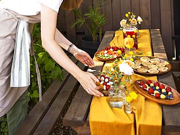 Wedding. Banquet. Chairs and a table for guests, decorated with candles, are served with cutlery and crockery and covered with yellow tablecloth. Waiter setting table stands on a green lawn in the backyard banquet area