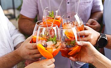 Happy friends spending time together, focus on young women drinking Aperol spritz cocktail. Summer wedding party. Happiness and celebration concept