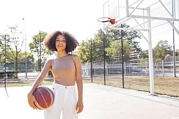 Mixed-race young smiling female outdoors and having fun. Stylish cool teen girl gathering at basketball court, playing basketball outdoors