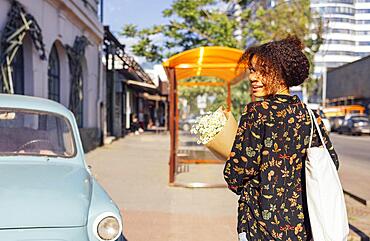 Young afro american woman holding flowers and smiling. Happy beautiful darkskin girl walks along the street with a bouquet of daisies. Positive model outdoors on on city summer background. Copy space