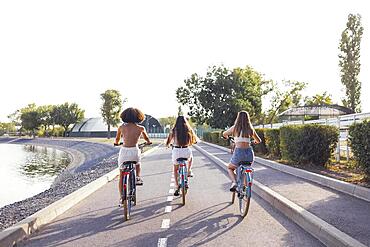 Teenagers of different nationalities and appearance on bicycles ride along a city street. Young and positive girls smile together. Healthy lifestyle and friendship concept