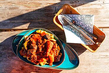 Plate of goulash with noodles and cutlery on a wooden table, Landgasthof zum Gruenen Baum, Ringenwalde village, Uckermark, Brandenburg, Germany, Europe