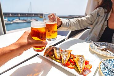 A couple toasting with beer by the sea eating fried fish, traditional Mediterranean food