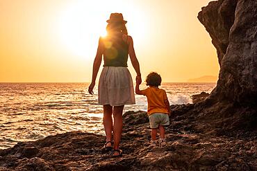 Mother and son at sunset on the beach of Tacoron on El Hierro, Canary Islands, vacation concept, orange sunset