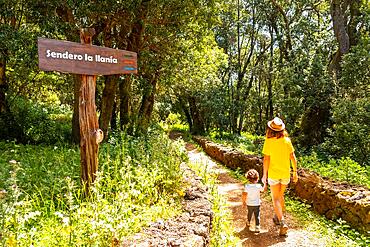 A mother with her son next to a sign identifying the La Llania trekking trail in El Hierro, Canary Islands. lush green landscape