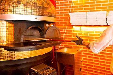 Artisan pizza oven. Chef introducing with the shovel, hot and ready pizza for customers