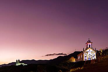 Image with baroque style illuminated churches on top of the hill in Ouro Preto, Minas Gerais illuminated during sunset