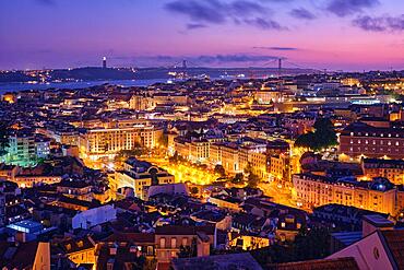 Night view of Lisbon famous view from Miradouro da Senhora do Monte tourist viewpoint of Alfama and Mauraria old city districts, 25th of April Bridge in the evening twilight. Lisbon, Portugal, Europe