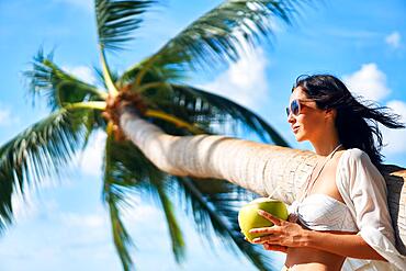 Beautiful young woman enjoy coconut drink and relax on tropical beach with palm tree. Summer vacation concept