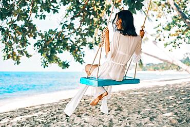 Carefree happy woman on swing on beautiful paradises beach. Relax and freedom concept