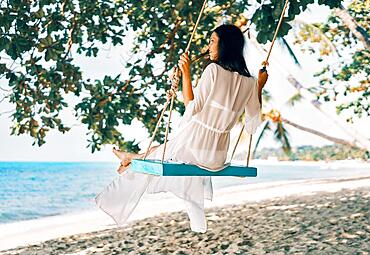 Carefree happy woman on swing on beautiful paradises beach. Relax and freedom concept