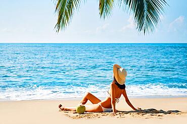 Young beautiful woman sunbathe and relax sitting alone on tropical beach. Summer vacation concept