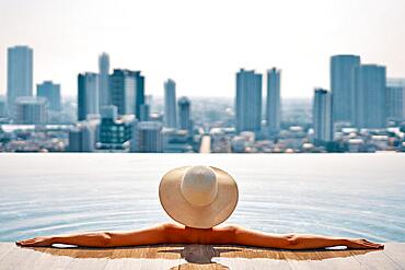 Pretty woman in hat relax in swimming pool on roof top enjoy cityscape panorama view. Vacation, summer and relax concept