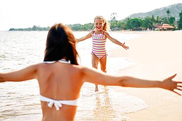 Happy little girl run to her mother for hugs on tropical beach. Summer vacation, happy family, love concept