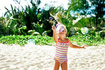 Little happy girl playing soap bubbles on the topical beach. Childhood, lifestyle concept