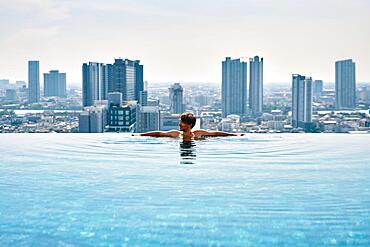 Young man relax on the edge of swimming pool in roof top of hotel. Summer vacation concept