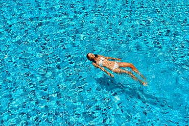 Top view of young woman swimming in clean turquoise water in infinity swimming pool. Relax, vacation, sport concept