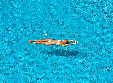 Top view of young slim woman in white bikini relax and floating in infinity swimming pool. Summer vacation, rest concept