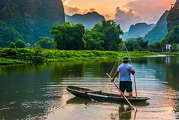 Fisherman on boat in Trang An, a scenic area near Ninh Binh, Vietnam inscribed as a UNESCO World Heritage Site in 2014