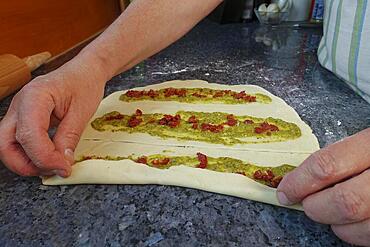 Swabian cuisine, preparation of hearty party yeast plait, salty yeast plait, yeast pastry, yeast yeast dough with herb paste and dried tomatoes, pesto, rolling up raw dough, vegetarian, men's hands, worktop, typical Swabian reinterpreted, traditional cuisine, food photography, studio, Germany, Europe