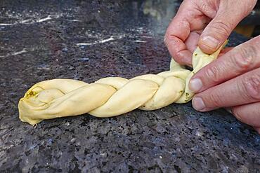 Swabian cuisine, preparing hearty party yeast plait, savoury yeast plait, yeast pastry, yeast yeast dough filled with herb paste and dried tomatoes, pesto, braiding raw dough, making plait from three strands, vegetarian, men's hands, worktop, typical Swabian reinterpreted, traditional cuisine, food photography, studio, Germany, Europe