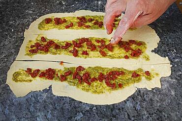 Swabian cuisine, preparing hearty party yeast plait, salty yeast plait, yeast pastry, filling yeast yeast dough with herb paste and dried tomatoes, pesto, raw dough, vegetarian, man's hand, worktop, teaspoon, typical Swabian reinterpreted, traditional cuisine, food photography, studio, Germany, Europe