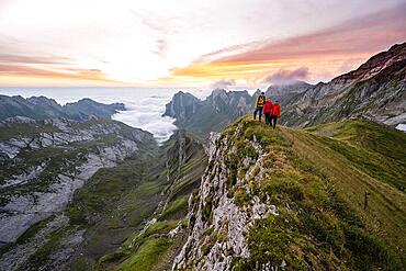 View over Saentis mountains into the valley of Meglisalp at sunrise, friends, mountaineers at Rotsteinpass, high fog in the valley, Saentis, Appenzell Ausserrhoden, Appenzell Alps, Switzerland, Europe