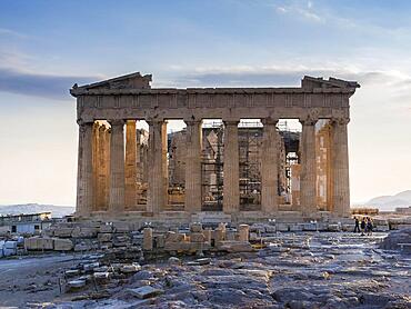 Frontal view of Parthenon on Acropolis, Athens, Greece against sunset, clear blue sky and few tourists taking photos of ruins