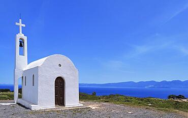 White Greek Orthodox chapel or church on hilltop of seashore against clear blue sky on sunny day. Traditional religious building. Typical Greek landscape. Diagonal composition, copyspace