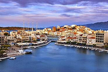 Colorful view of Voulismeni lake and Agios Nikolaos town on Crete island, Greece at sunset. Boats, cafes, restaurants, ship, marina, promenade