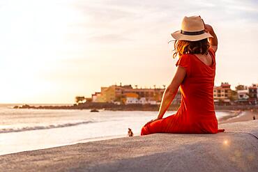 Tourist woman at sunset enjoying vacations on the beach of Valle Gran Rey village in La Gomera, Canary Islands. Sitting looking at the sea