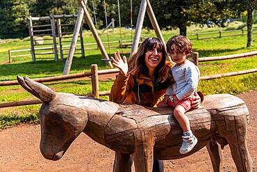 A boy and a mother playing on the wooden horse in the leisure area at Laguna Grande in the Garajonay natural park on La Gomera, Canary Islands