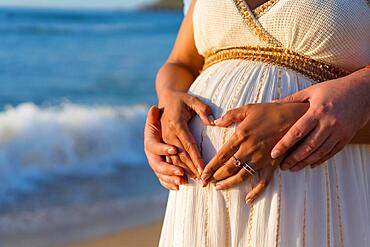 Pregnant maternity latin woman on the beach at sunset, maternity concept