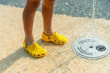 Children enjoying summer pool with water jets, summer vacation. Yellow child's flip flops