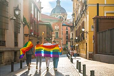 Man with his back facing the demonstration with rainbow flags at sunset, gay pride party in the city, lgbt concept