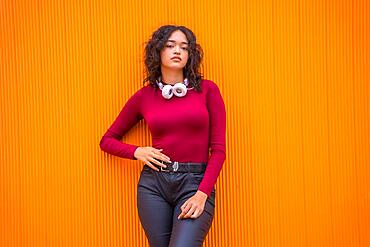 Portrait of latin woman with headphones, technology concept on an orange background, student on campus