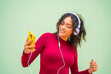 Portrait of latin woman with headphones smiling, technology concept on a green background, listening to music