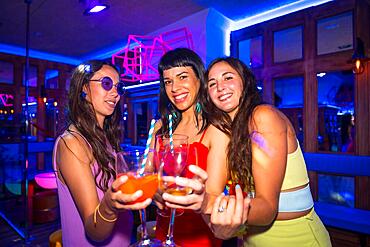 Portrait attractive women toasting with glasses at nightclub at summer night party in pub