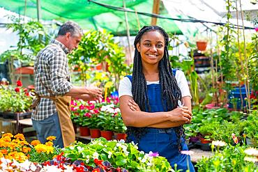 Happy black ethnic woman flower and plant nursery worker cutting plants in greenhouse