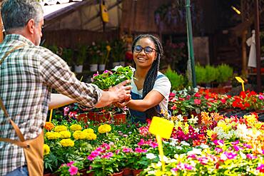 Happy female customer buying flowers from a gardener in a nursery inside the greenhouse