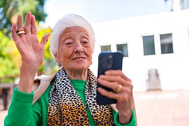 An elderly man in the garden of a nursing home or retirement home on a sunny summer day, looking at the phone, technologies in the elderly