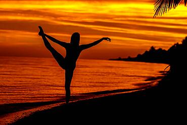 The sun rises over the Gulf of Mexico near Sinanche Yucatan Mexico with a nude latin model posing against the colorful sky